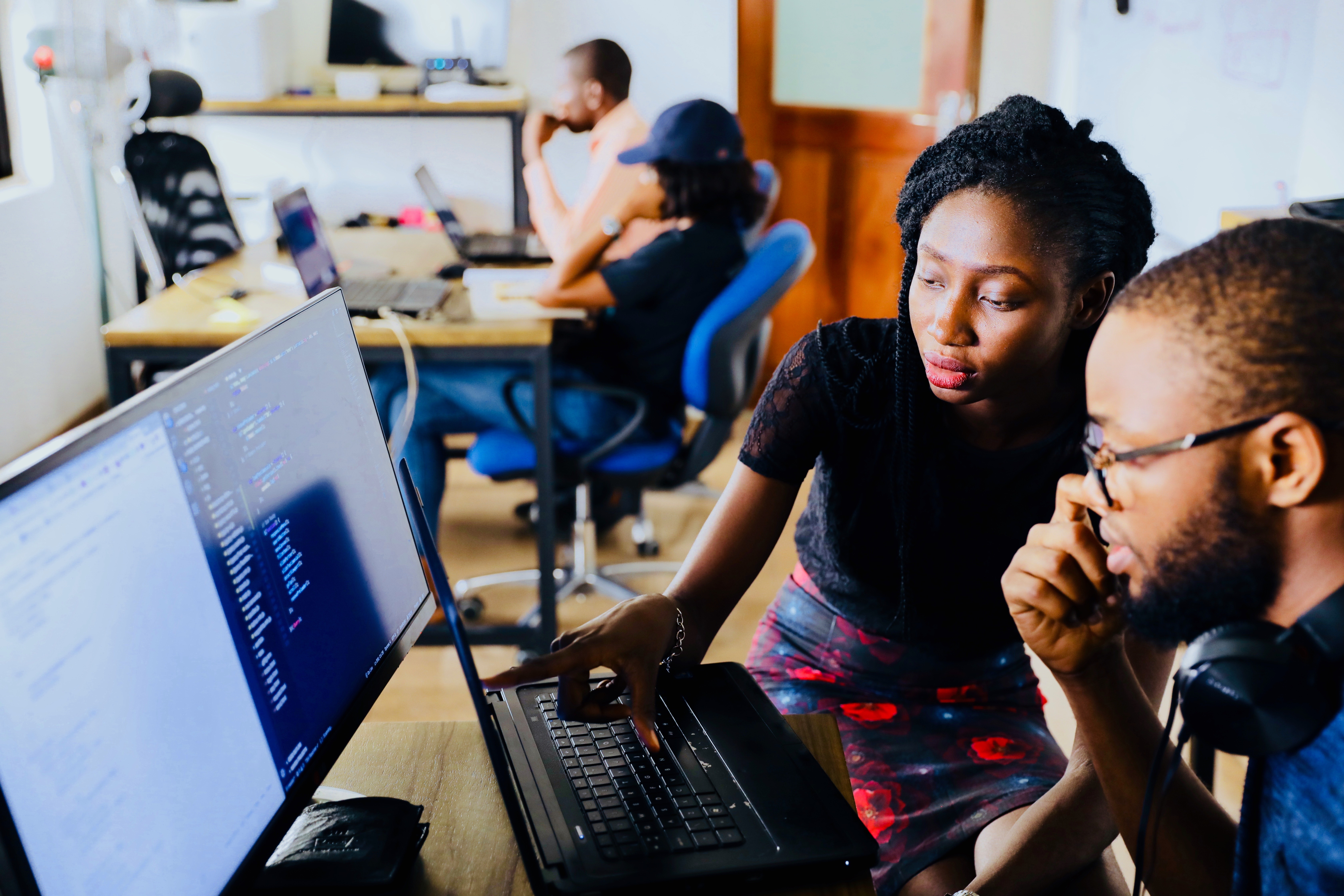 four employees working on computers. There are two Black women and two Black men.