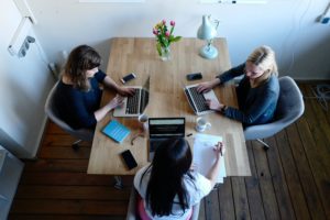 Three women sitting at a table together working on laptops.