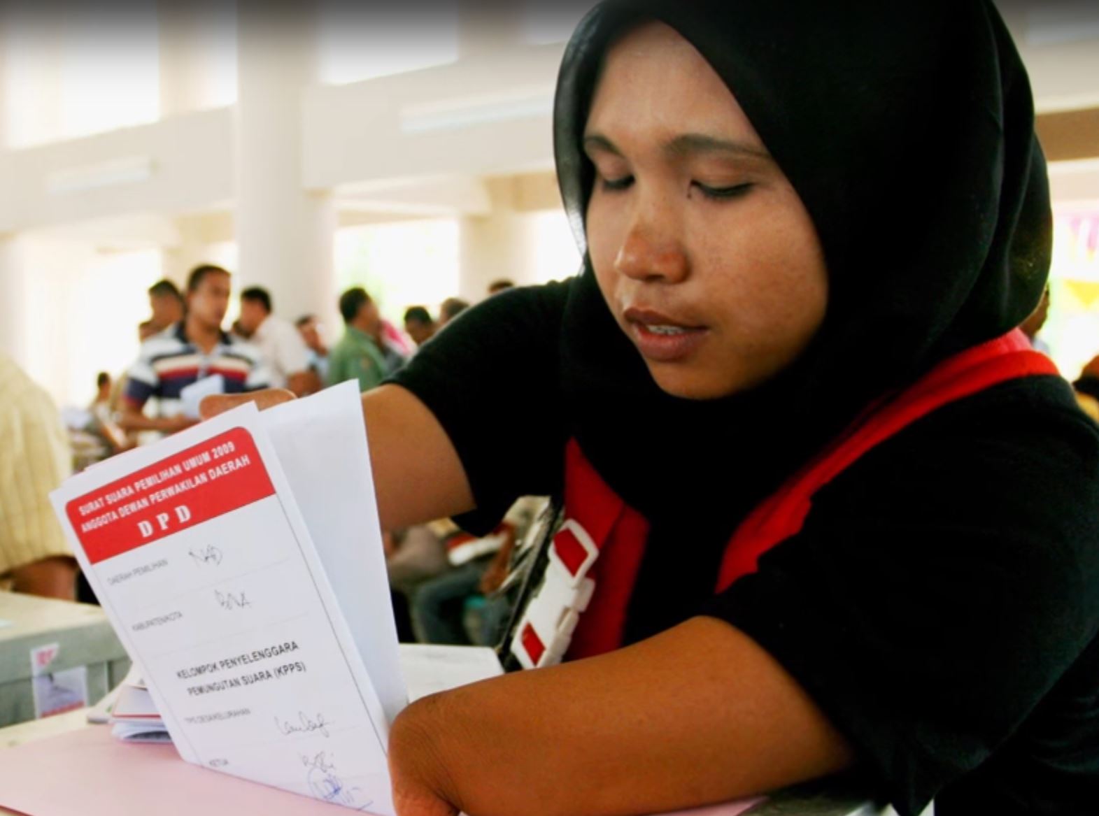 Young woman in a head scarf placing her ballot in the ballot box.
