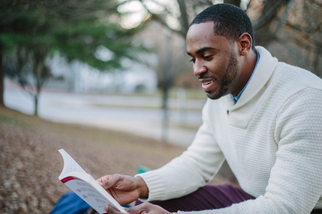 Man sitting outside, looking engaged in reading the open book he holds in front of him.