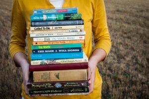 A woman holding a stack of different books.