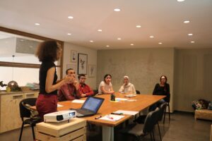 A woman is speaking to five colleagues around a table.