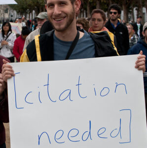 Man holding a sign saying citation needed