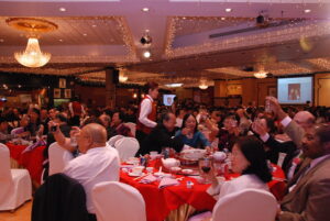 A large crowd of people at a restaurant raising their glasses