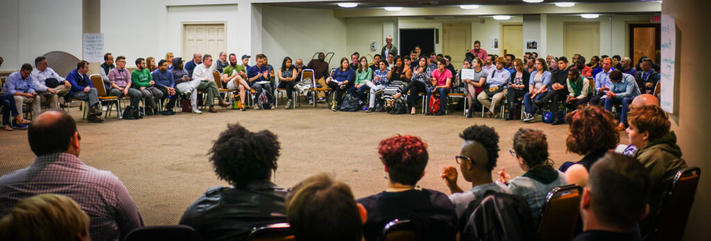 A crowd of people sitting in a large circle, holding a meeting.