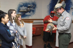 A park ranger holding an armadillo explains something to a group of students