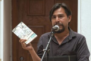 Man speaking into a microphone and holding up a book