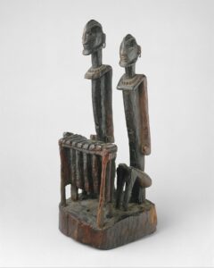 Wooden sculpture of two figures seated at a balafon instrument, which looks like a xylophone or a marimba.