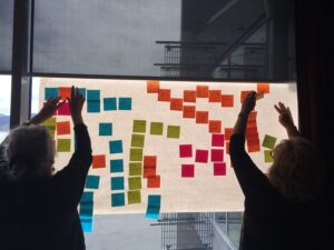 Two women arrange sticky notes on a window