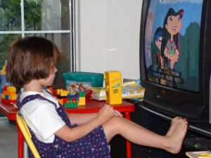 Girl sitting in front of TV with feet up, watching a cartoon.