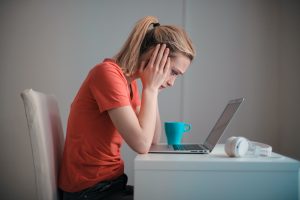 A student sitting at her laptop starting at it with her head in her hands.