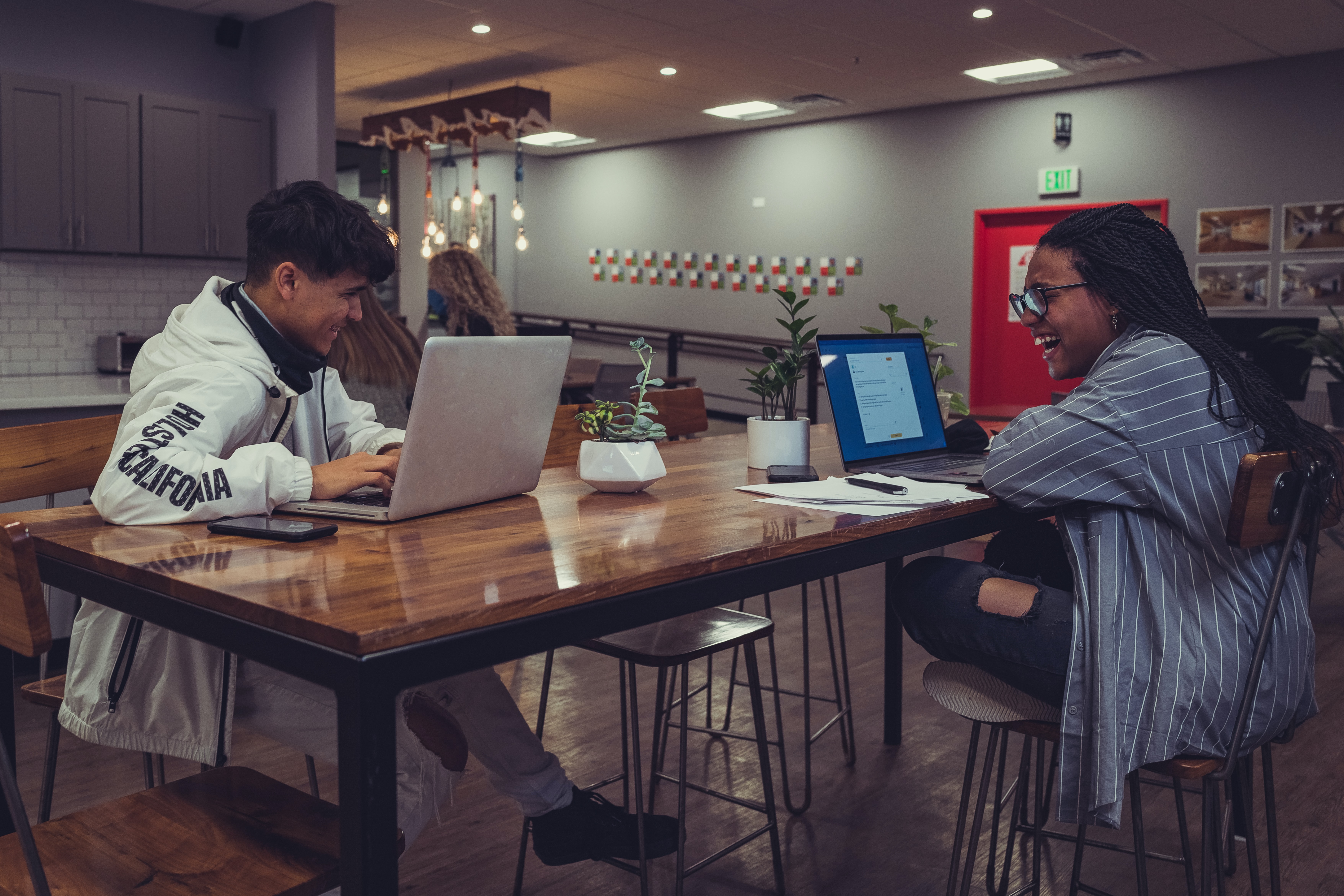 Two students laughing together during a research session with their laptops.