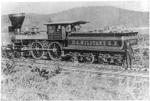 A black and white photograph that shows the Gen. Haupt locomotive and five men posed inside the car and outside near the railroad tracks.