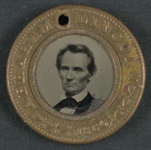 An Abraham Lincoln-Hannibel Hamlin campaign button from the 1860 election. The button has a black and white photo of Abraham Lincoln in the center. 