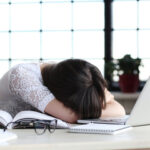 Woman working at laptop with her head on her arms in frustration