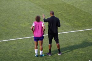 One person coaching another on a soccer field