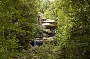 An architecturally modern house built over a stream in a forest.