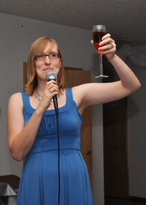 A woman giving a toast with a glass of wine in one hand and a microphone in the other