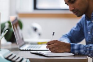 Person reading on computer and writing in a notebook 