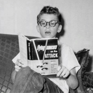 Boy reading book called flying saucers on the attack. He looks shocked 