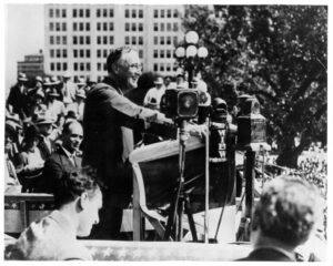 FDR leans on a podium while standing to give a campaign speech in Topeka, Kansas