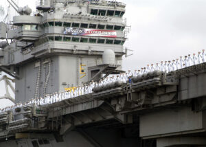 Hundreds of soldiers in white standing underneath a Mission Accomplished banner.