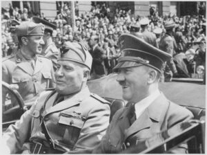 A photograph of Adolf Hitler and Benito Mussolini talking in a car with a large crowd behind them.