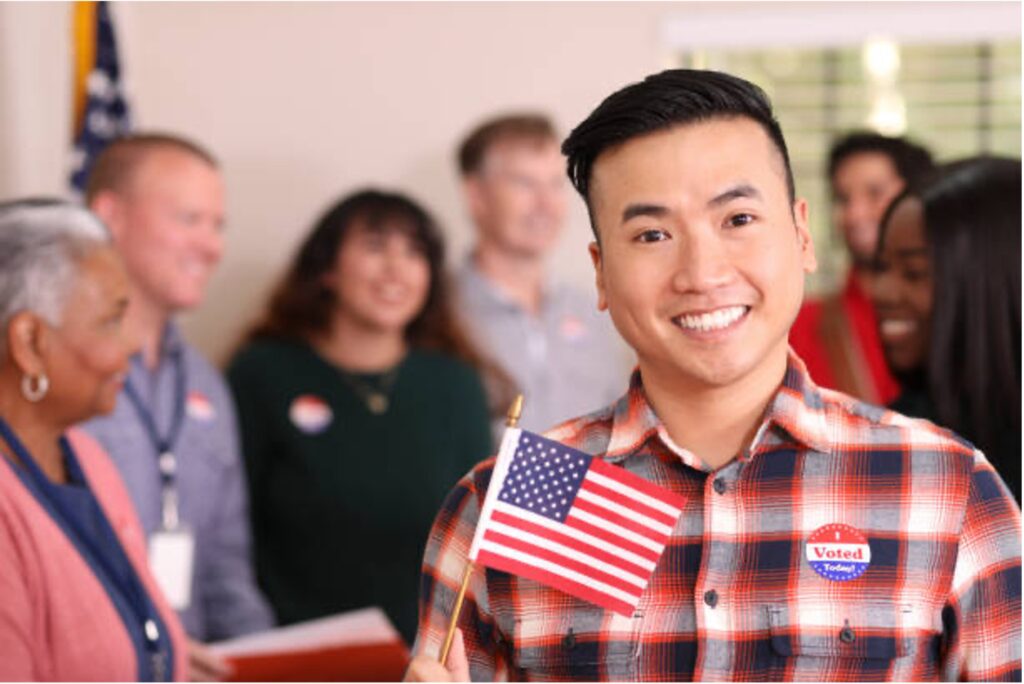 A smiling person holding an American flag and wearing an "I Voted" sticker.