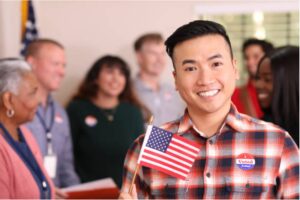 A smiling person holding an American flag and wearing an "I Voted" sticker.