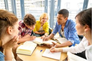 Five people gathered around a table with open books on it.