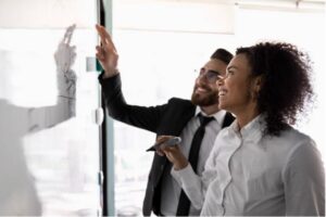 Two people smiling and looking at a whiteboard
