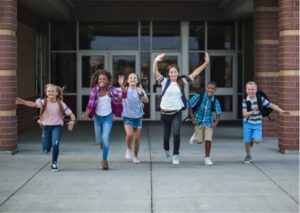 Children with backpacks on smiling and running out of a building