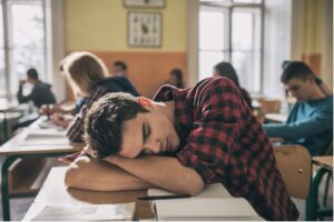 A student napping on a desk in a classroom.
