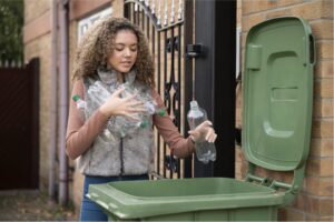 A girl throwing plastic bottles in a bin outside.