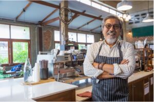 A man wearing an apron smiling in a cafe.