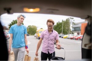 Two people putting things in the back of a car