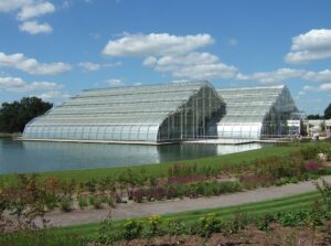 A large, commercial greenhouse sits at the edge of water, with a path shown crossing the image in the lower foreground.