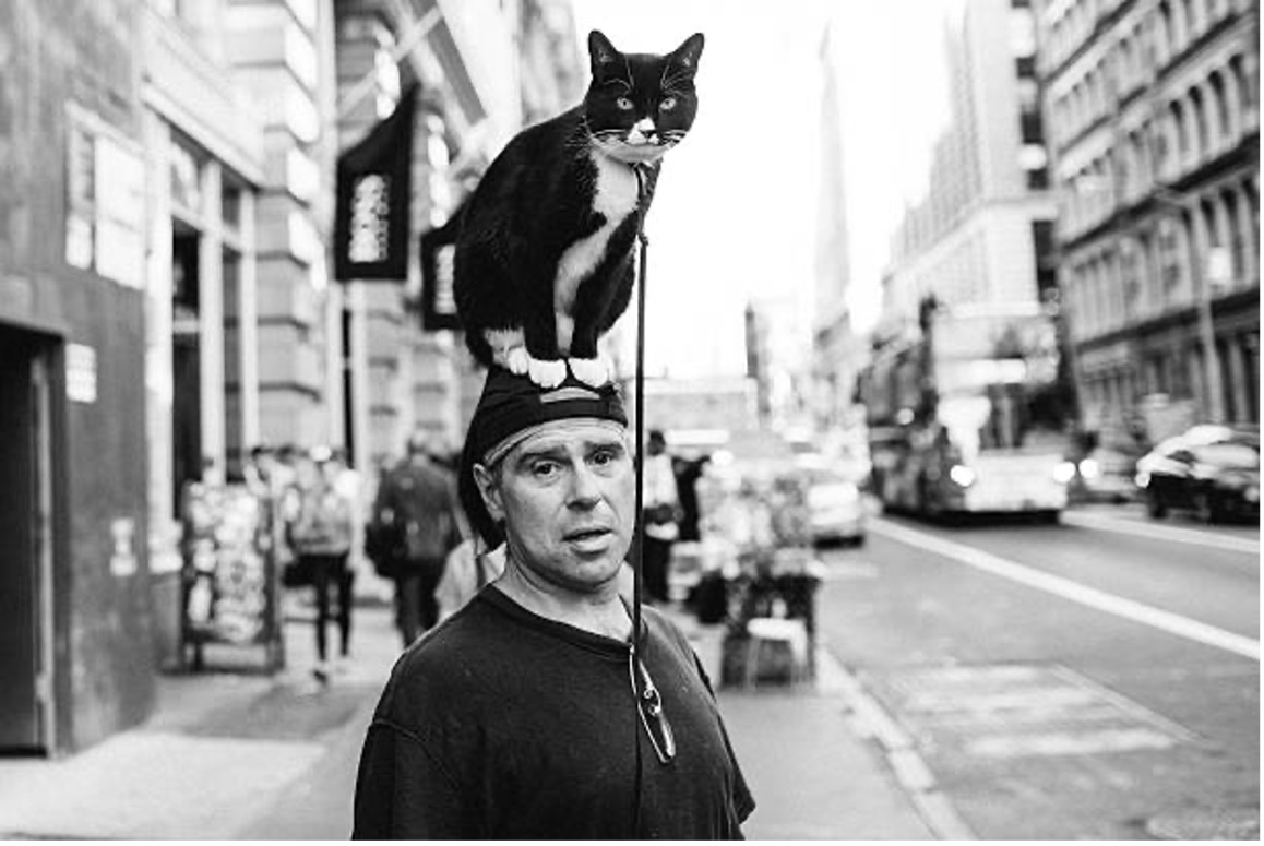Black and white photo of a man with a cat on his head.