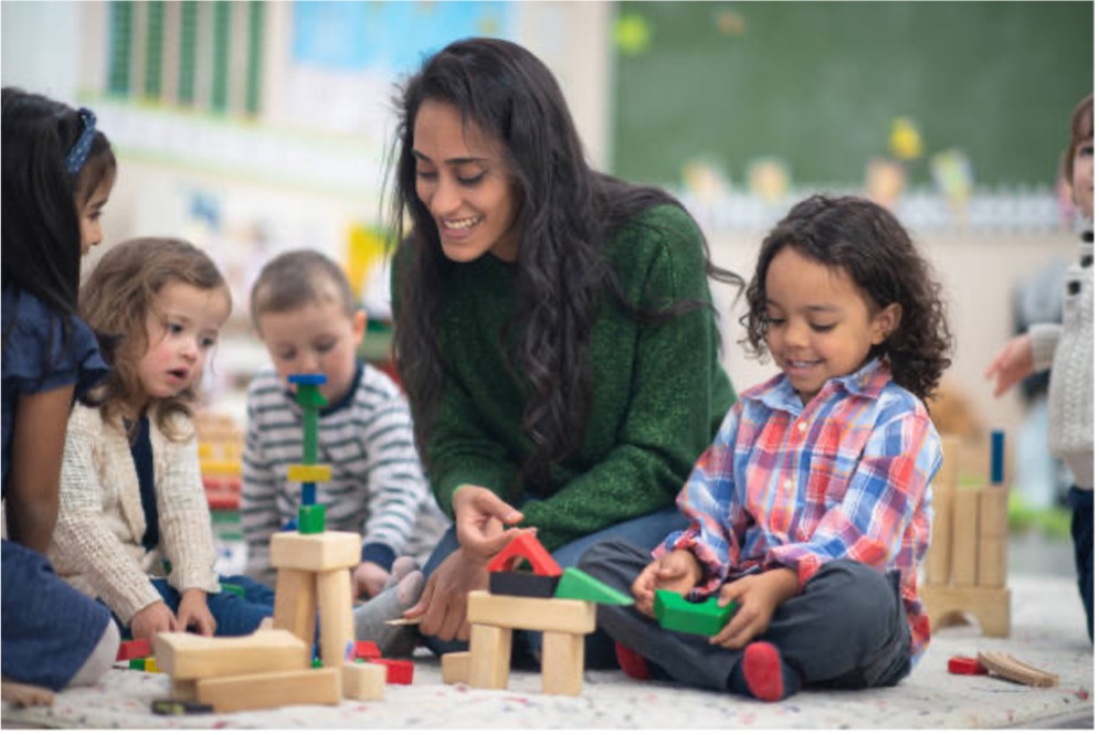 A woman playing with blocks with a group of children.
