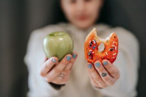 person holding an apple and a donut that has a bite taken from it