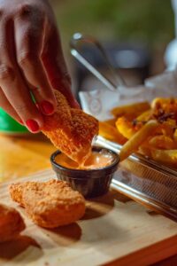 person's hand is dipping a chicken nugget into sauce