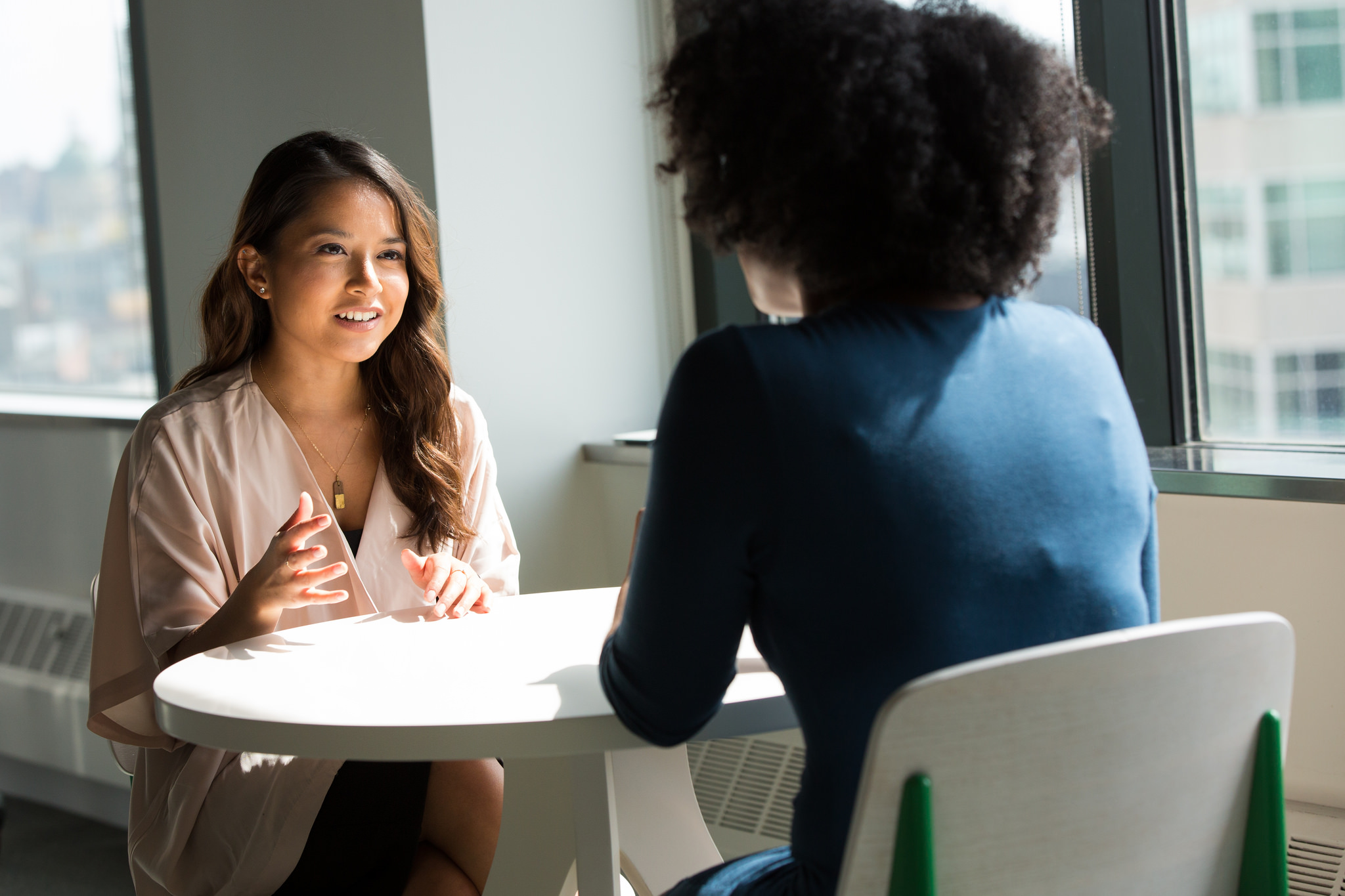 Two professionally-dressed woman sitting at a table engaged in a job interview.