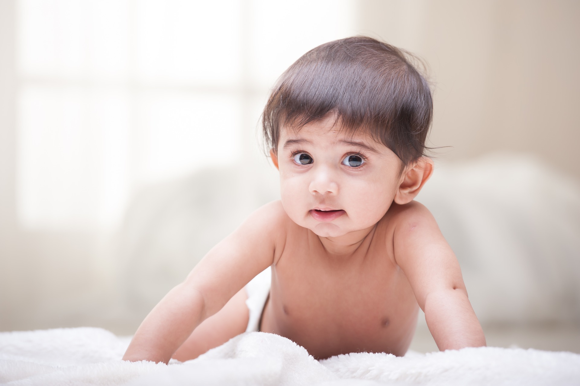 Young baby, around 6 months old, doing tummy time and looking happily at the camera.