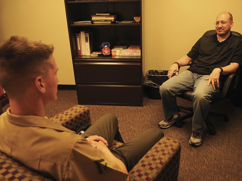 A therapist and patient sit across from each other in chairs in an office.