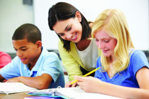 Teacher looks on as two fourth-grade students work on assignments.