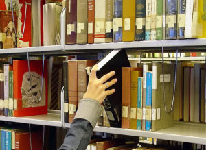 Hand reaching for a book on a bookshelf.