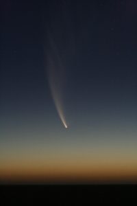 Image shows distant comet falling toward the ground with a sunset sky.