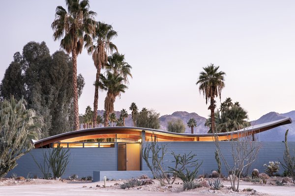 Viewed from the curb, Wave House, now painted a soft blue, showcases a curvilinear roof mimicking the mountainous landscape behind. The wave's canopy is anchored at four corners by beams supported by steel posts and installed with clerestory windows, emphasizing renewal for the midcentury form.