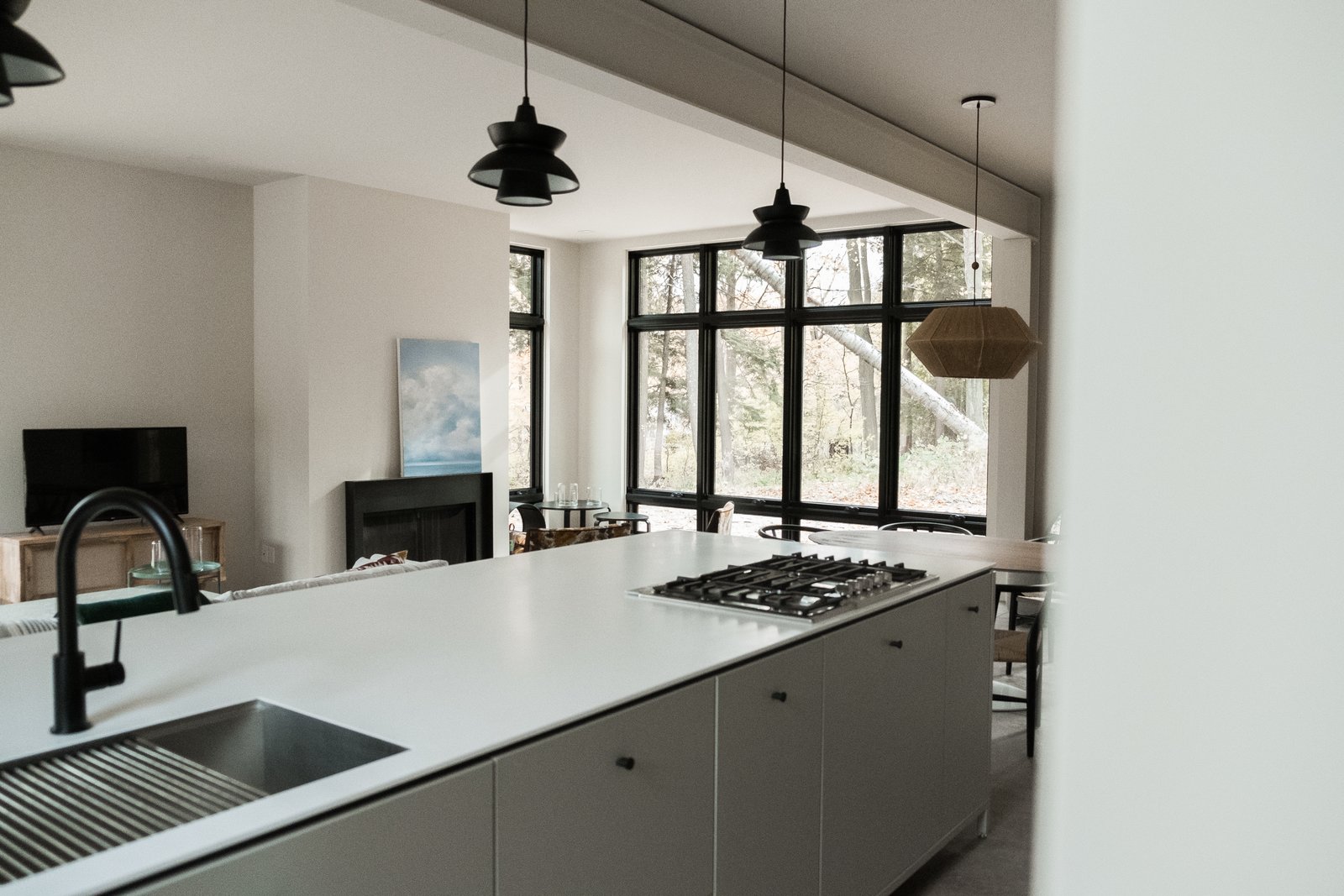View from kitchen island to great room with steel mantel fireplace and floor-to-ceiling windows.