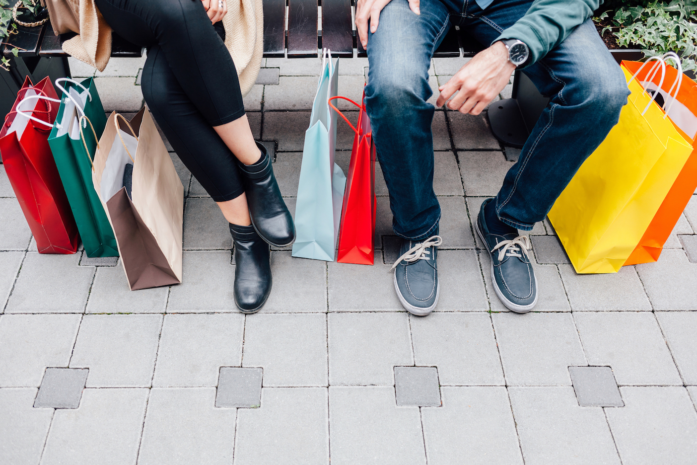 Image of two people resting on a bench with shopping bags
